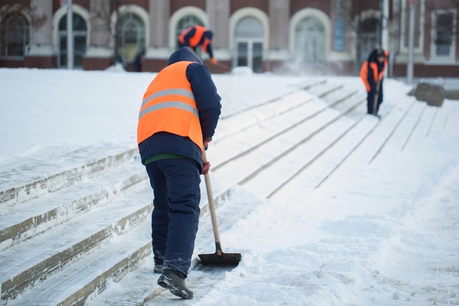 Mitarbeiter räumen Schnee von Treppen und Wegen im Winterdienst vor öffentlichem Gebäude